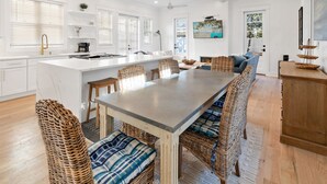 A modern kitchen with white cabinets, a large island, and a dining area with wicker chairs and a long table.