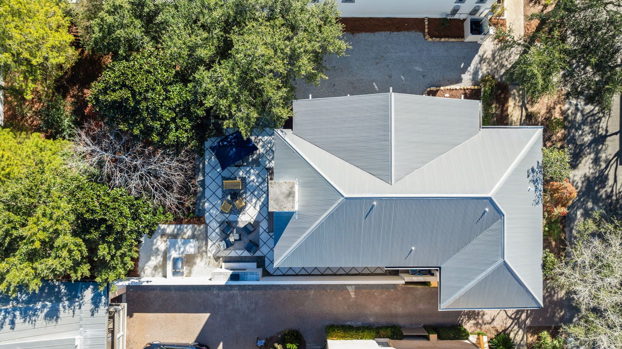 Vista aérea de uma casa moderna com design geométrico no telhado, um pátio com móveis de exterior e vegetação ao redor.