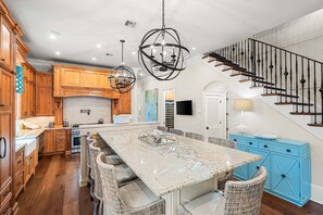 A spacious kitchen with wooden cabinets, a marble island, wicker chairs, and a blue cabinet. - Elegant Camp District Home with Electric Cart, 6 Bikes & Watercolor Beach Club Access (Santa Rosa Beach)