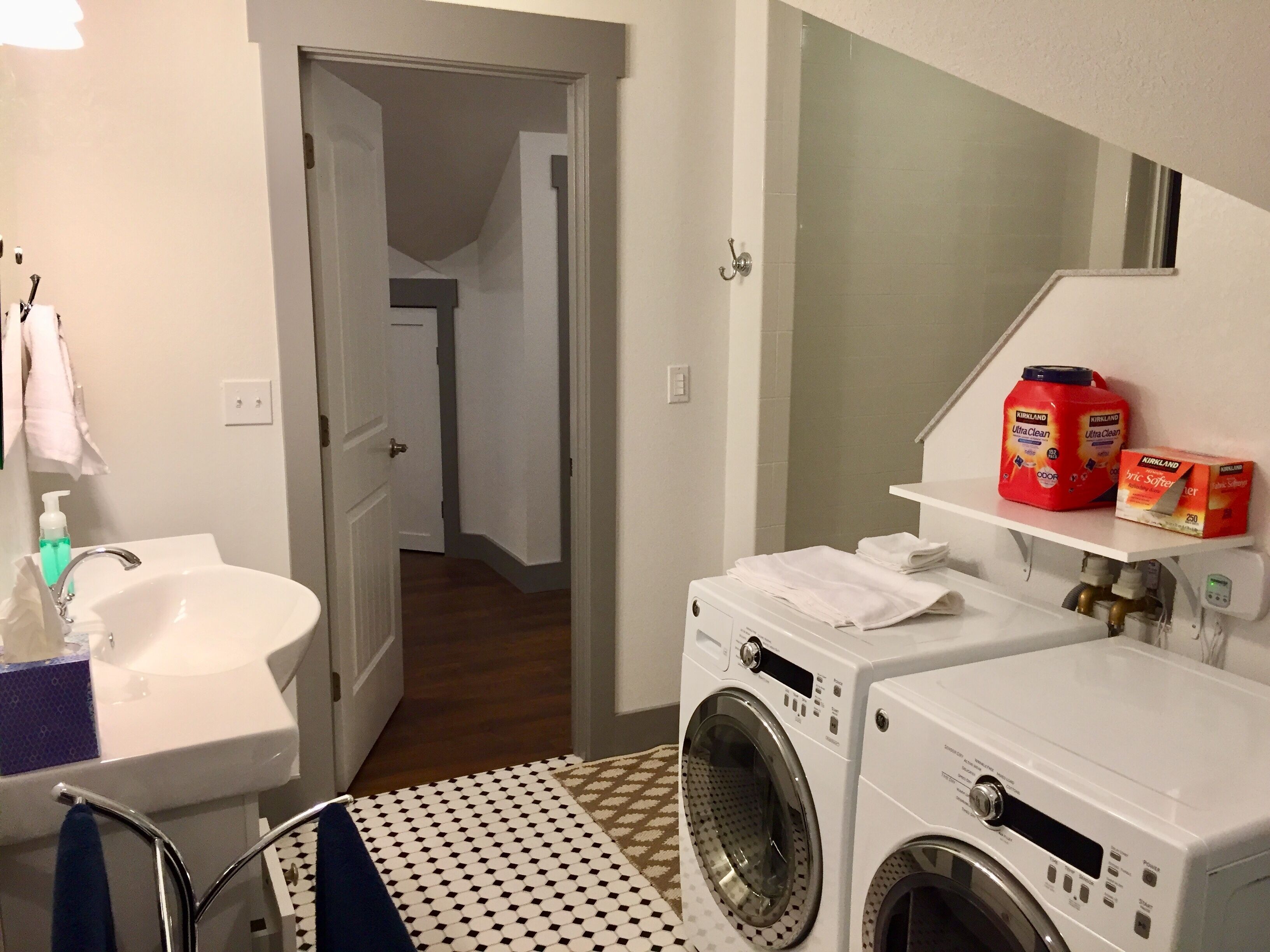 A laundry area with a washing machine, a sink, and a shelf with detergent bottles.