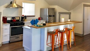 Una cocina moderna con una isla central, electrodomésticos de acero inoxidable y taburetes de bar color naranja.