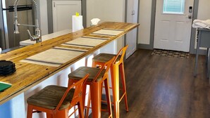 Una cocina con una isla grande, cuatro taburetes naranjas, un lavamanos de acero inoxidable y una puerta con ventana.