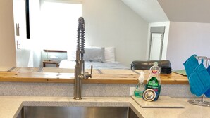 Una cocina con un lavamanos de acero inoxidable, un microondas y una encimera con una botella de detergente.