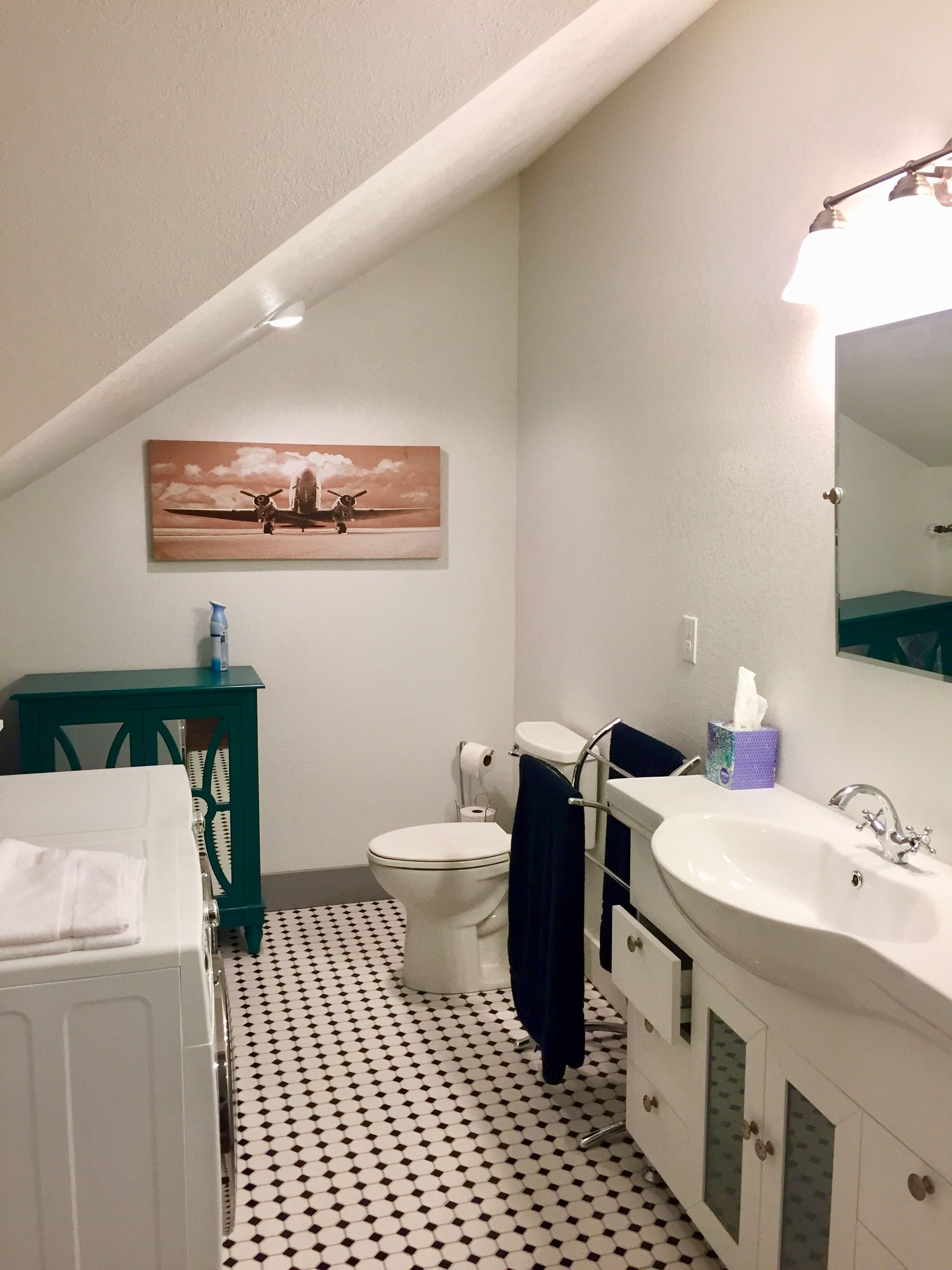 A bathroom with a white toilet, a sink, and a mirror. There is a painting on the wall and a patterned floor.