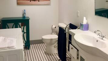 A bathroom with a white toilet, a sink, and a mirror. There is a painting on the wall and a patterned floor.