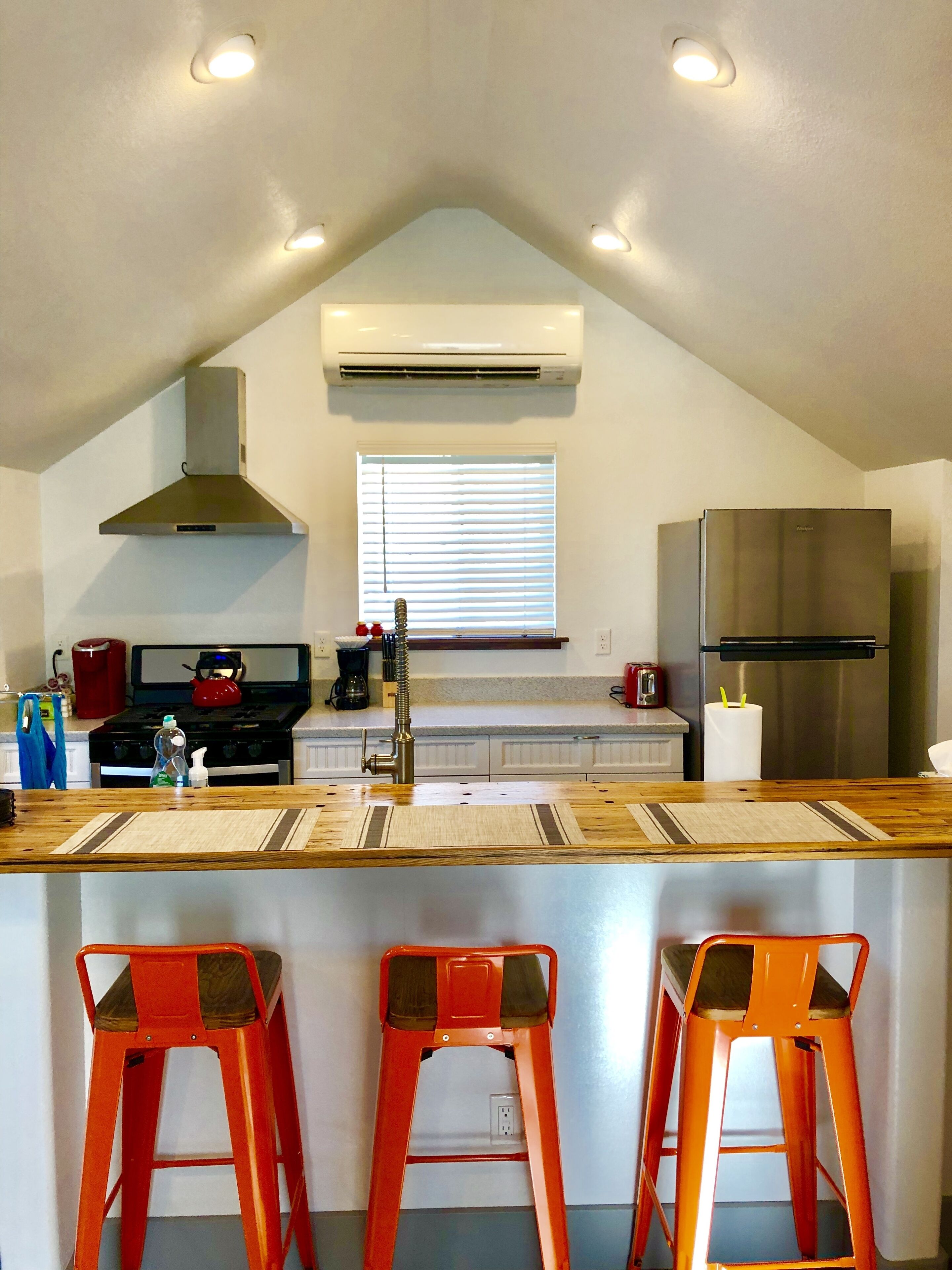 A modern kitchen with a central island, a stainless steel refrigerator, and a window with blinds.