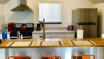 A modern kitchen with a central island, a stainless steel refrigerator, and a window with blinds.