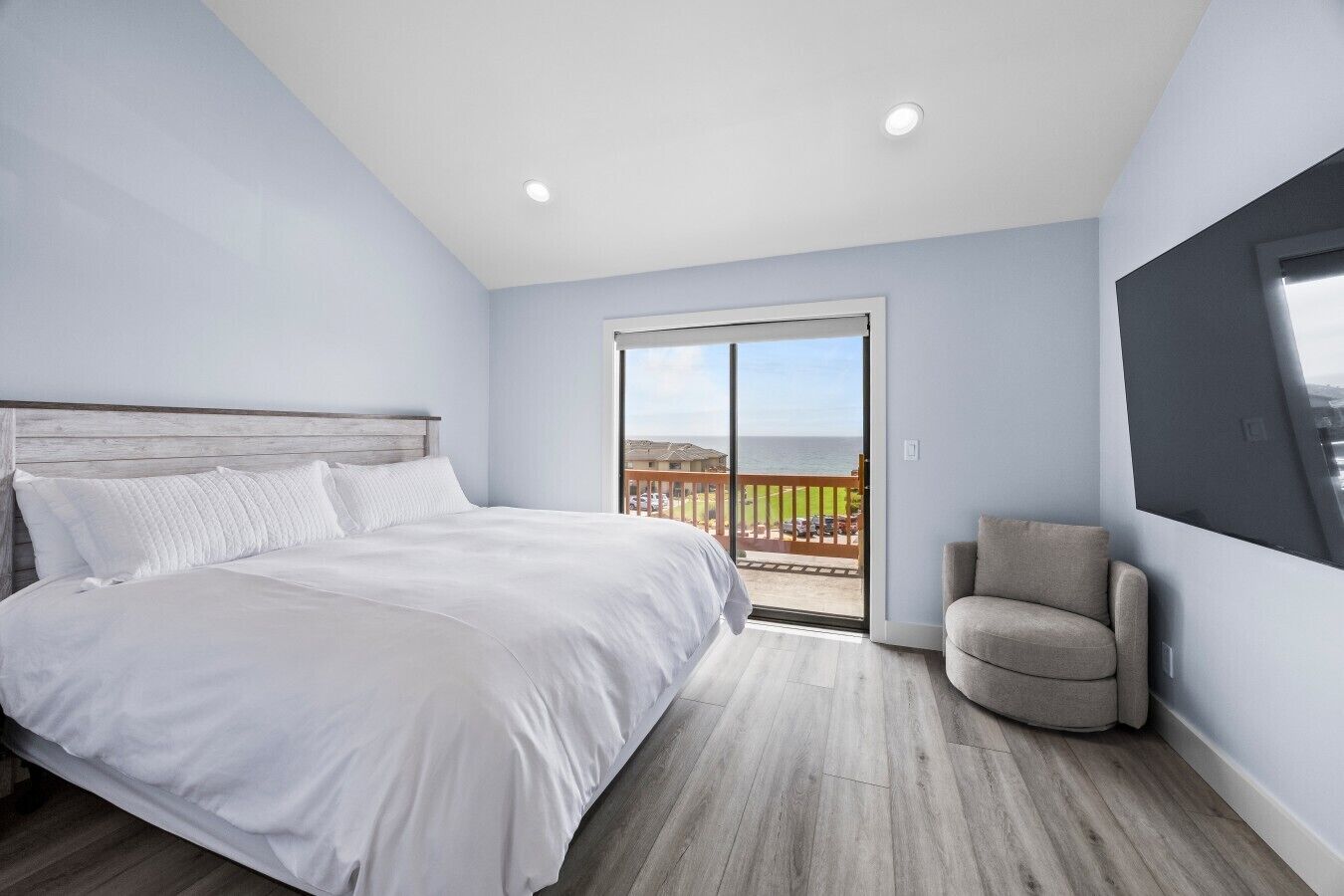 A bedroom with a bed, a chair, and a balcony with a view.