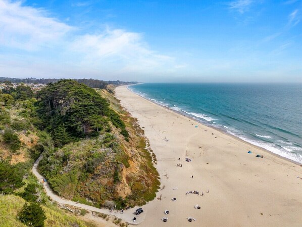 A coastal beach with a dirt path, beachgoers, and ocean views.