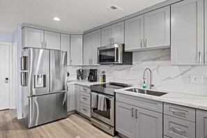 A modern kitchen with stainless steel appliances, grey cabinetry, and a marble backsplash.