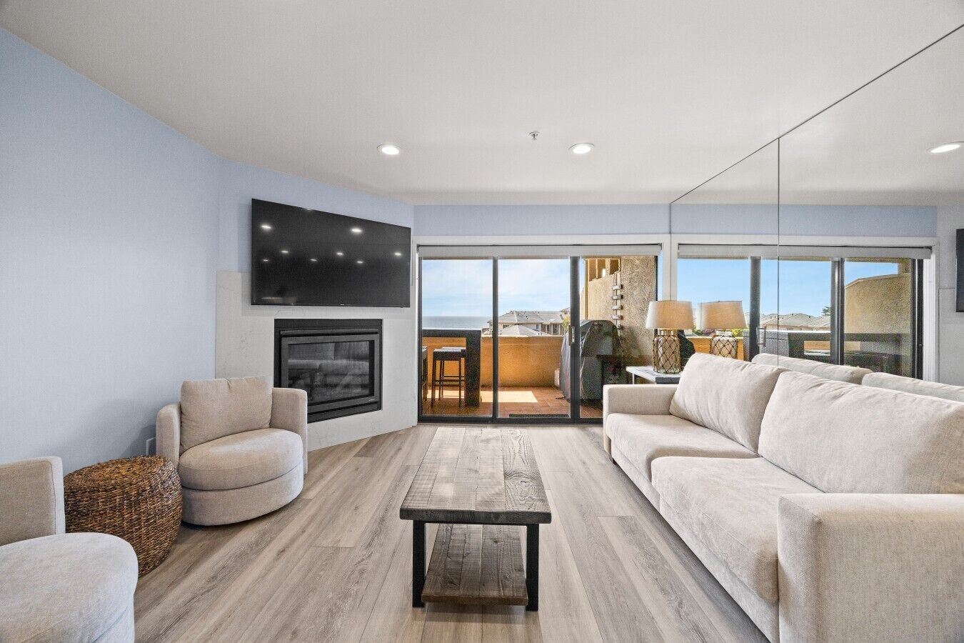 A modern living room with a fireplace, a flat-screen TV, and a large window offering a view of the outdoors.