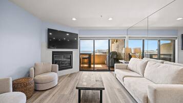 A modern living room with a fireplace, a flat-screen TV, and a large window offering a view of the outdoors.
