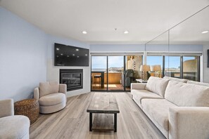 Een moderne woonkamer met een open haard, een flatscreen televisie en een groot raam met uitzicht op de omgeving.