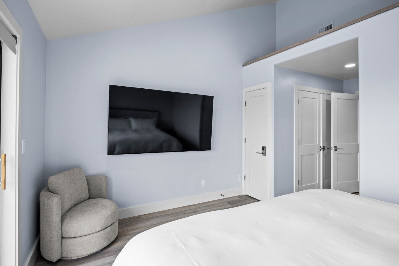 A bedroom with a bed, a chair, a wardrobe, and a wall-mounted television.