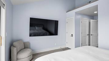 A bedroom with a bed, a chair, a wardrobe, and a wall-mounted television.