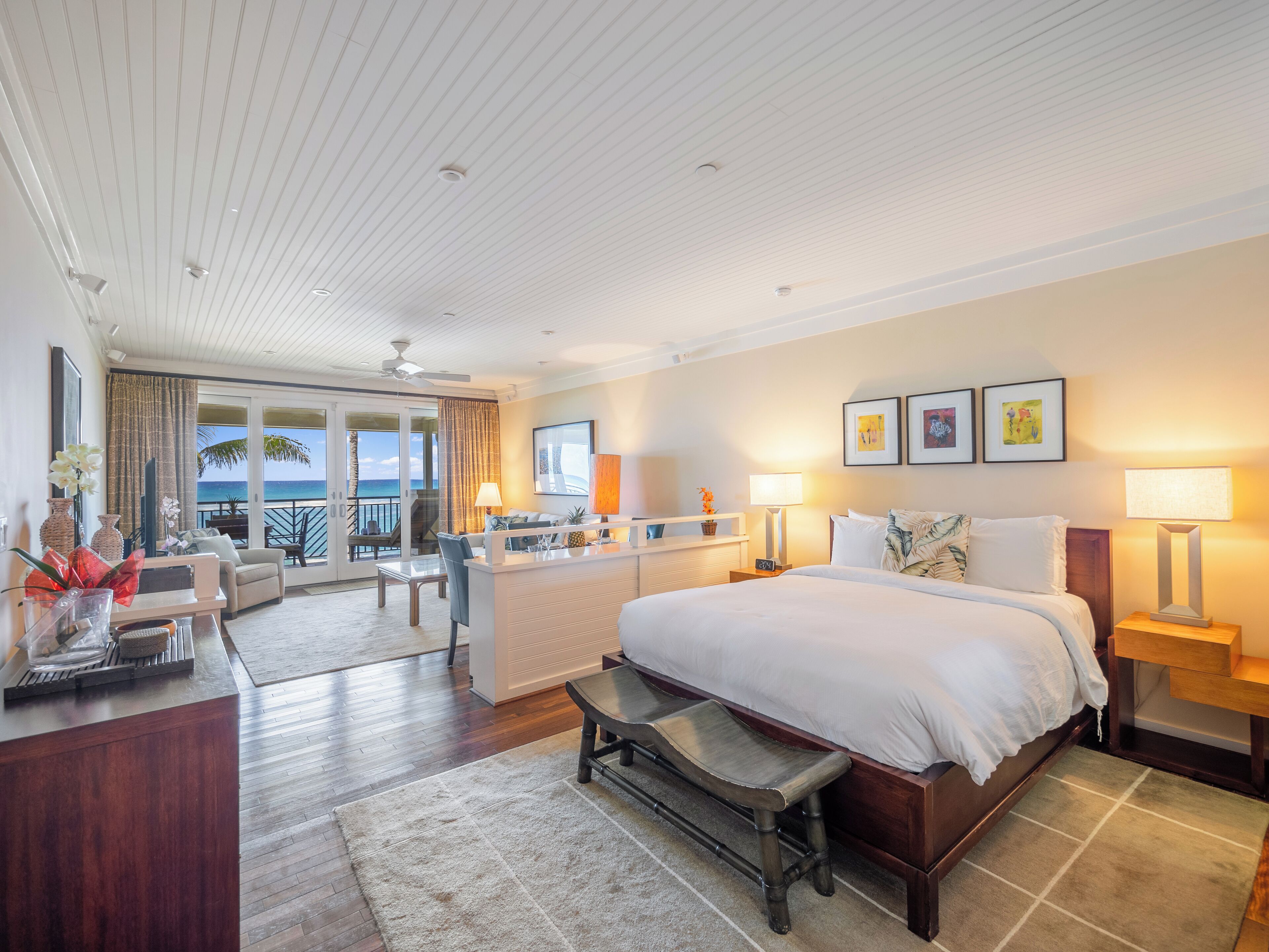 A spacious hotel room with a large bed, a desk, and a balcony with a view of the ocean.