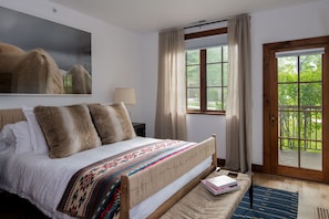 Quarto com cama grande, janela com cortinas, porta para uma varanda e um quadro na parede.
