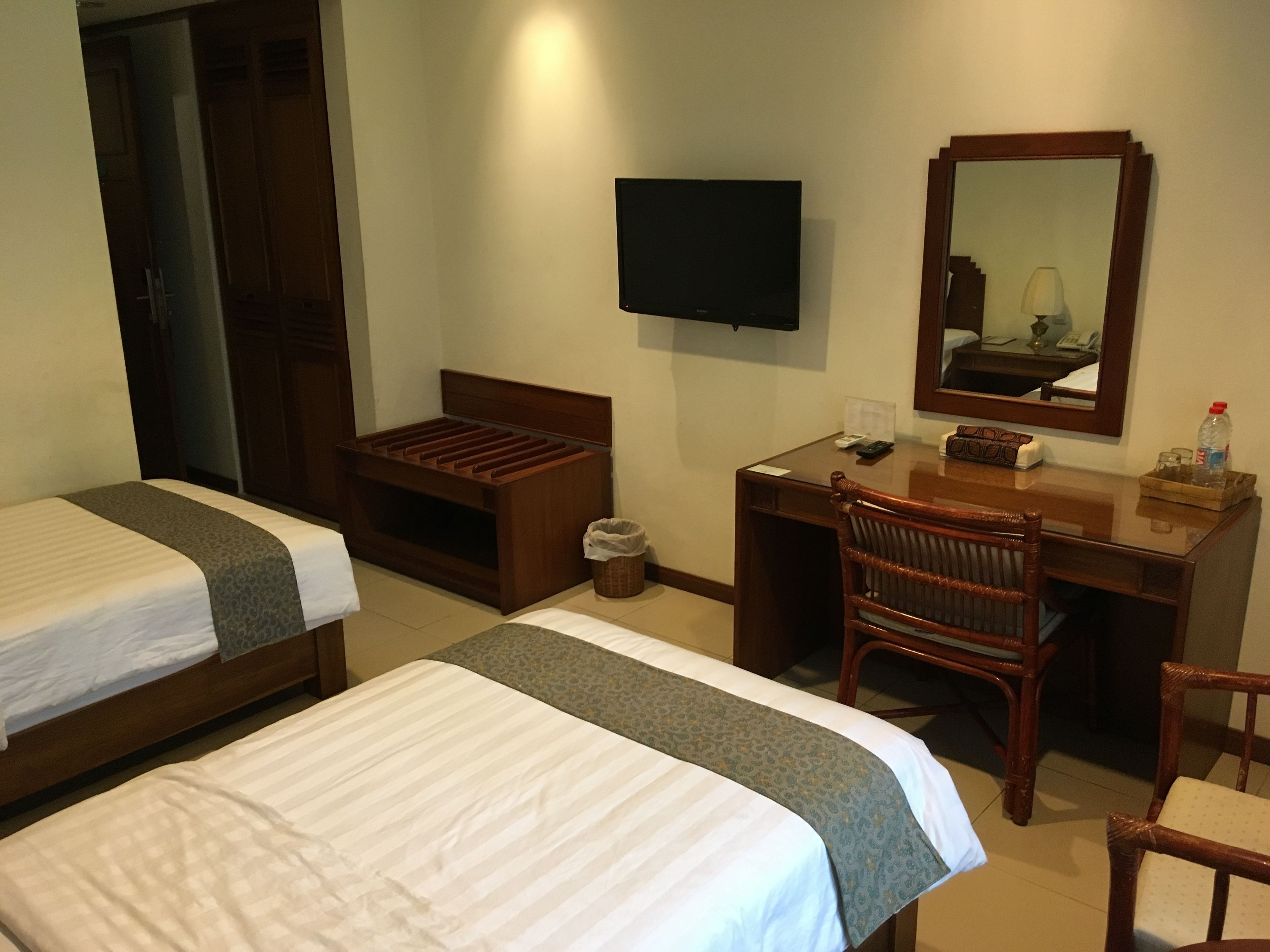 A hotel room with two single beds, a desk with a chair, a TV, and a mirror.