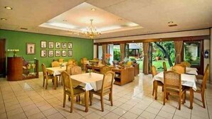Uma sala de jantar com várias mesas e cadeiras, um lustre e quadros nas paredes.