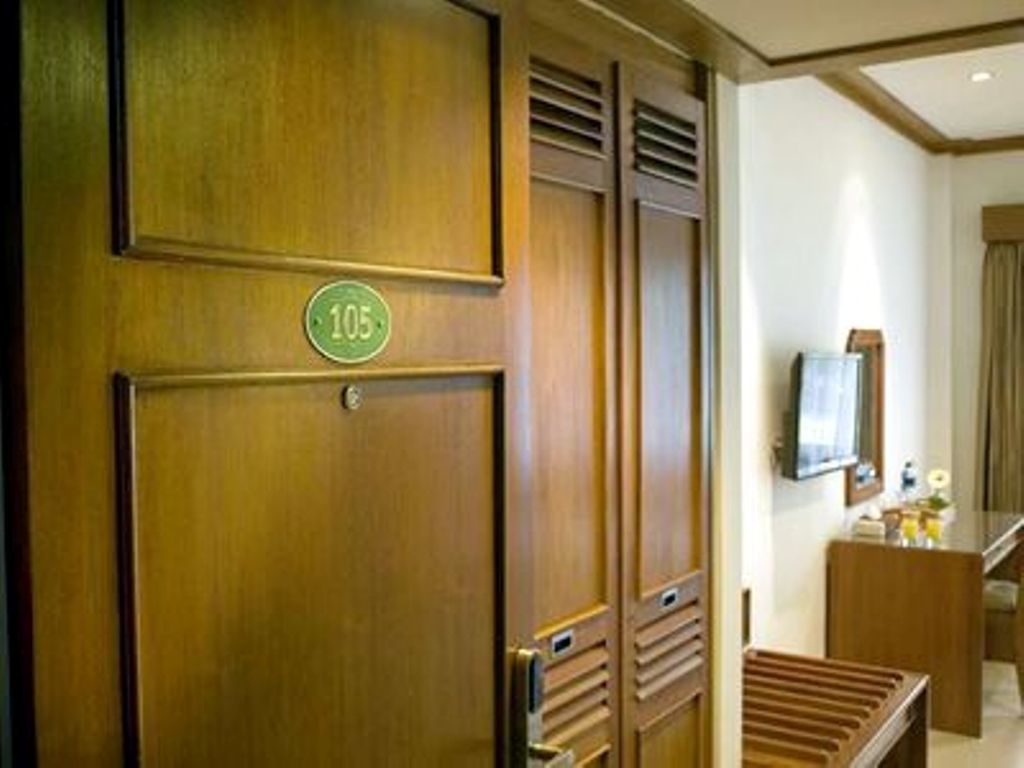 Une chambre d’hôtel avec une porte en bois portant le numéro « 105 », un téléviseur fixé au mur et un banc en bois.