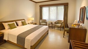 Quarto de hotel com uma cama grande, duas poltronas, uma mesinha e uma escrivaninha com espelho.