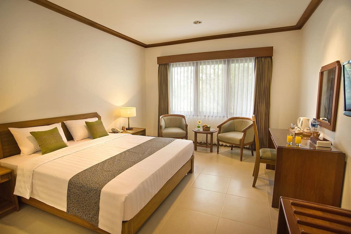 A hotel room with a large bed, two armchairs, a small table, and a desk with a mirror.