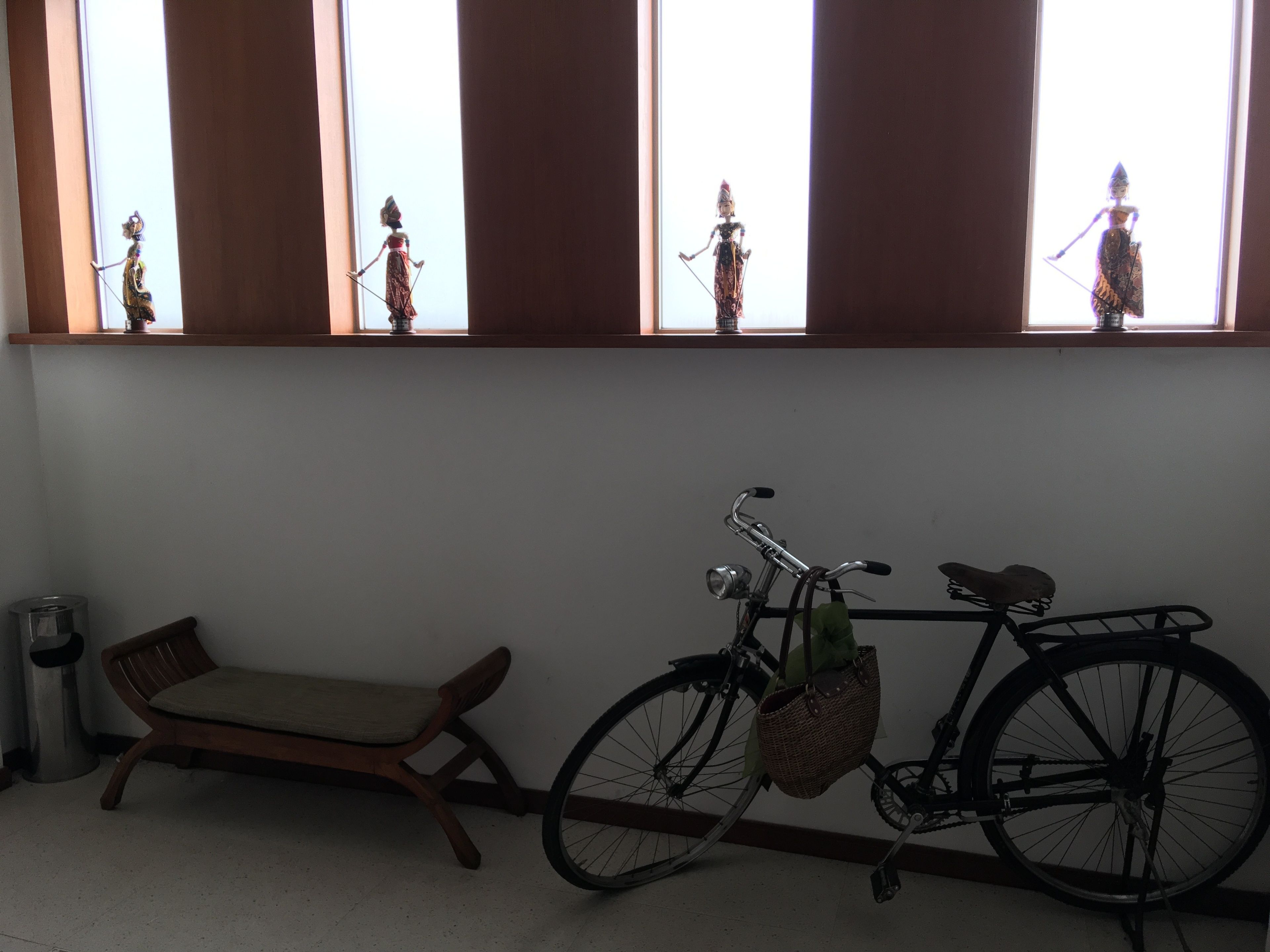 Ein Zimmer mit einer hölzernen Bank, einem Fahrrad mit Korb und einem Fenster mit Dekorationen.