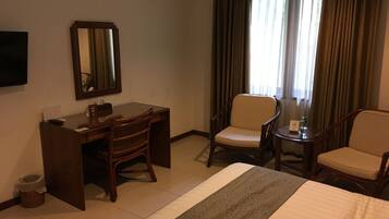 A hotel room with a bed, a desk, two chairs, a mirror, and a window with curtains.