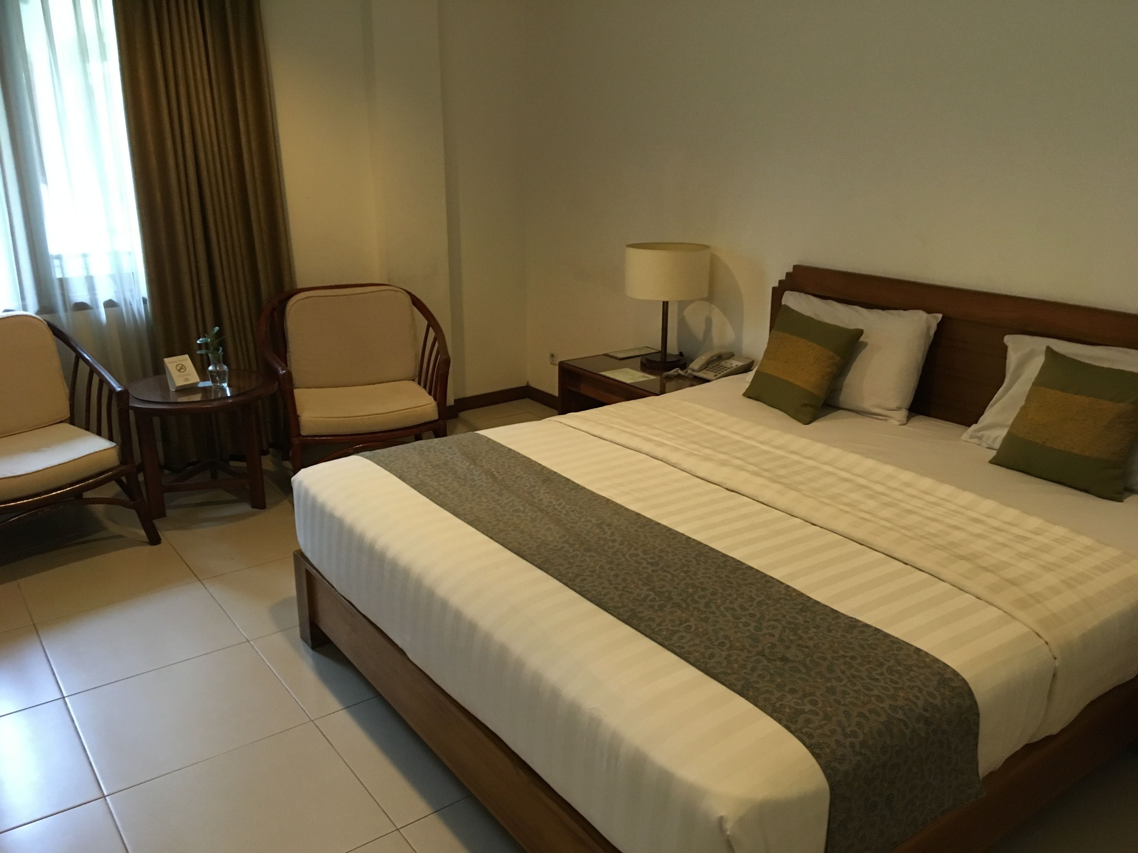 A hotel room with a large bed, a chair, a small table with a lamp, and a nightstand with a phone.