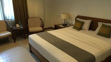 A hotel room with a large bed, a chair, a small table with a lamp, and a nightstand with a phone.