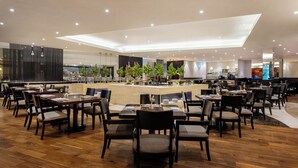 A modern restaurant with wooden flooring, dark chairs, and a central bar area. - Gulf Executive Residence (Manama)