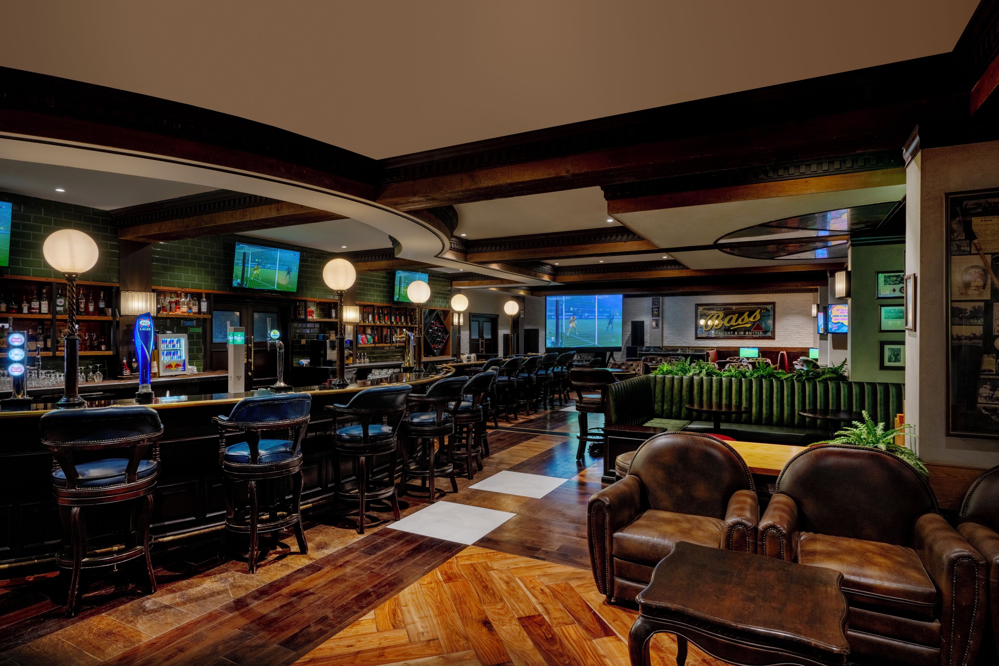A bar area with multiple seating options, including bar stools and tables, and a television screen displaying a sports event.