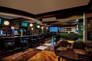 Zona de bar con distintas opciones de asientos, incluyendo taburetes y mesas, y una pantalla de televisión mostrando un evento deportivo.