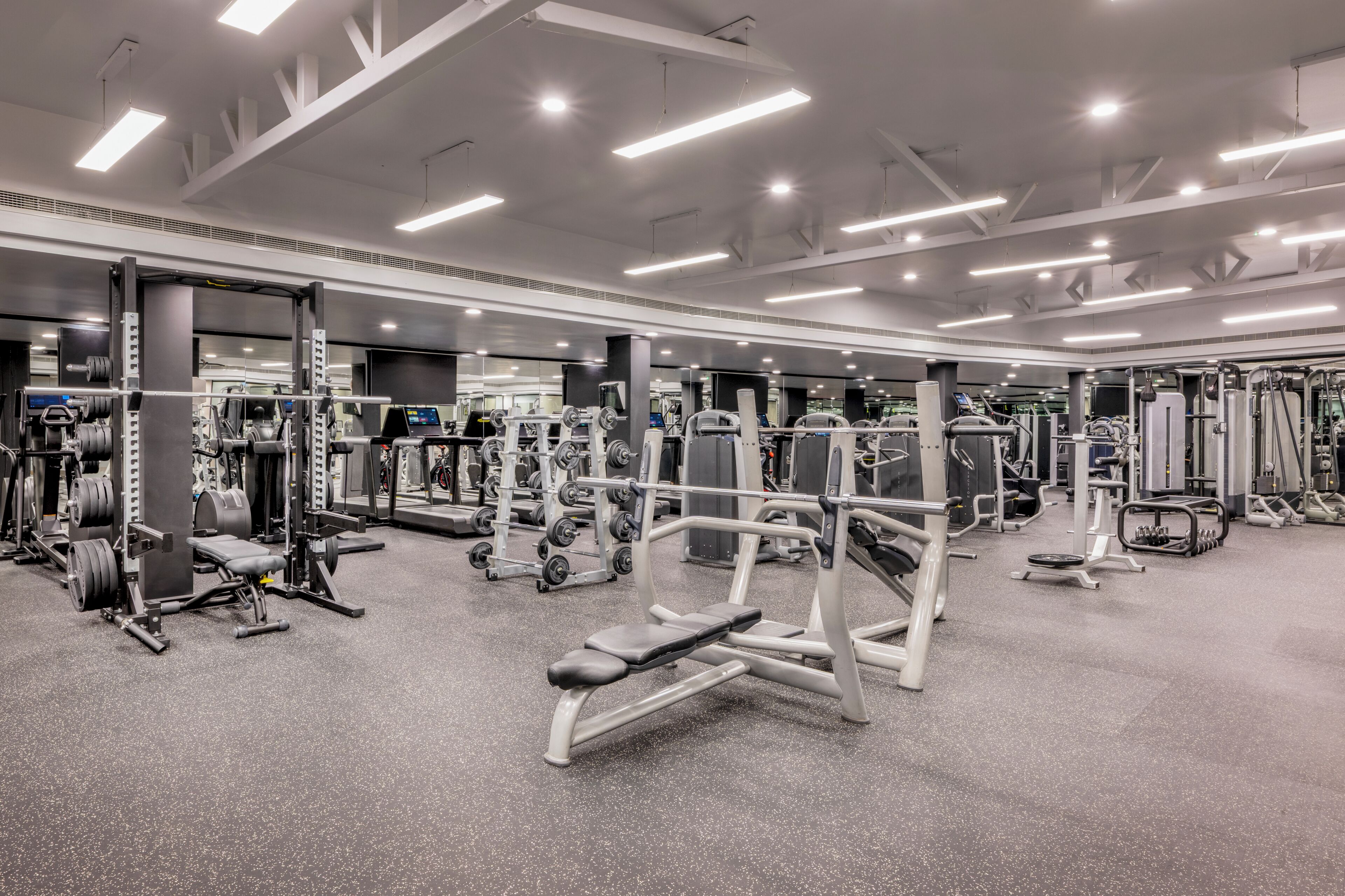 A well-lit gym with various exercise equipment and a speckled grey floor.