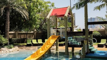 A pool area with a yellow slide, palm trees, and a red-roofed structure.