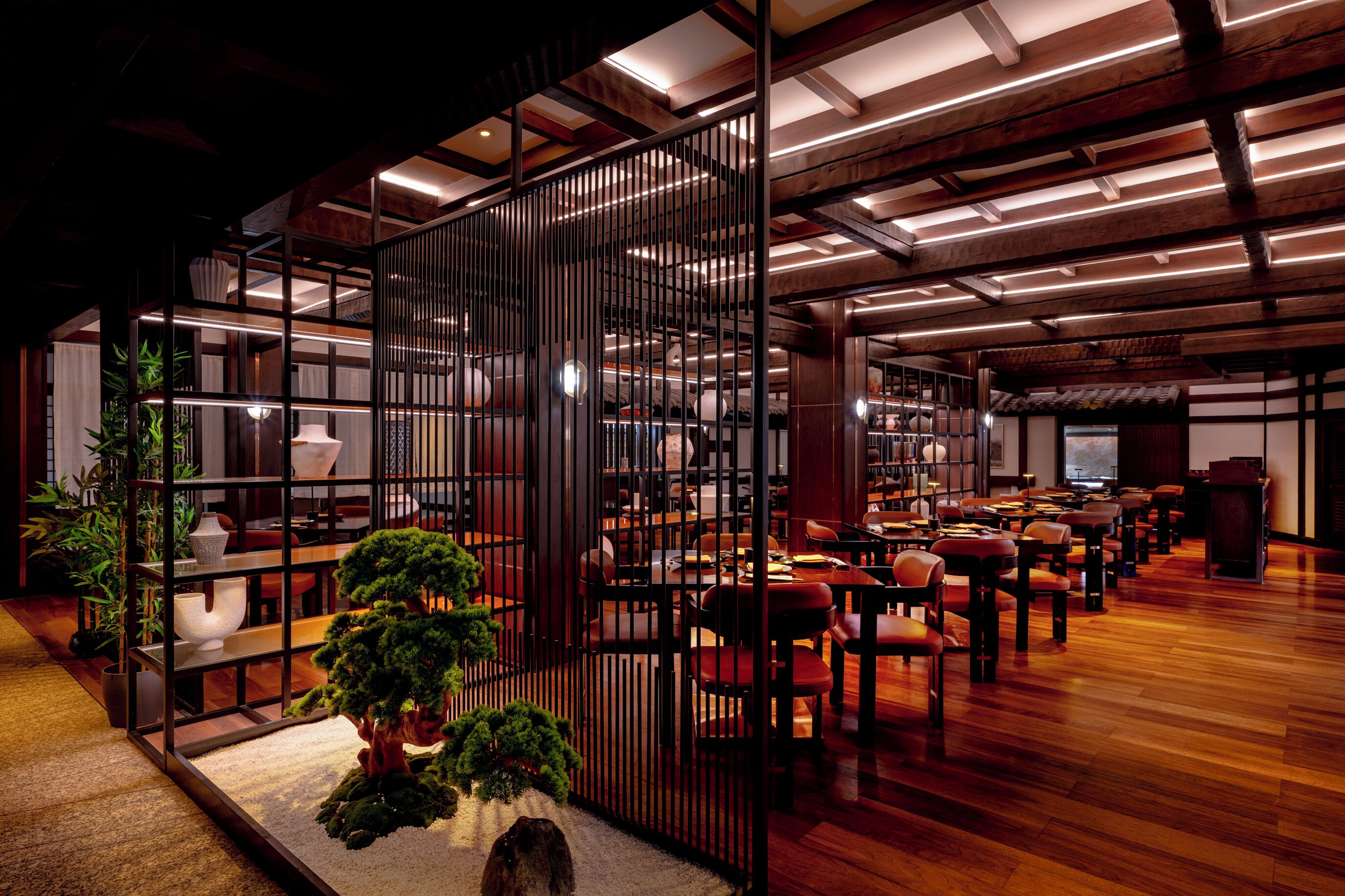 A spacious indoor area with wooden flooring, multiple seating arrangements, and a central decorative plant.