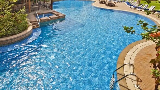 A large, curved swimming pool with lounge chairs and a covered seating area. - Gulf Executive Residence (Manama)