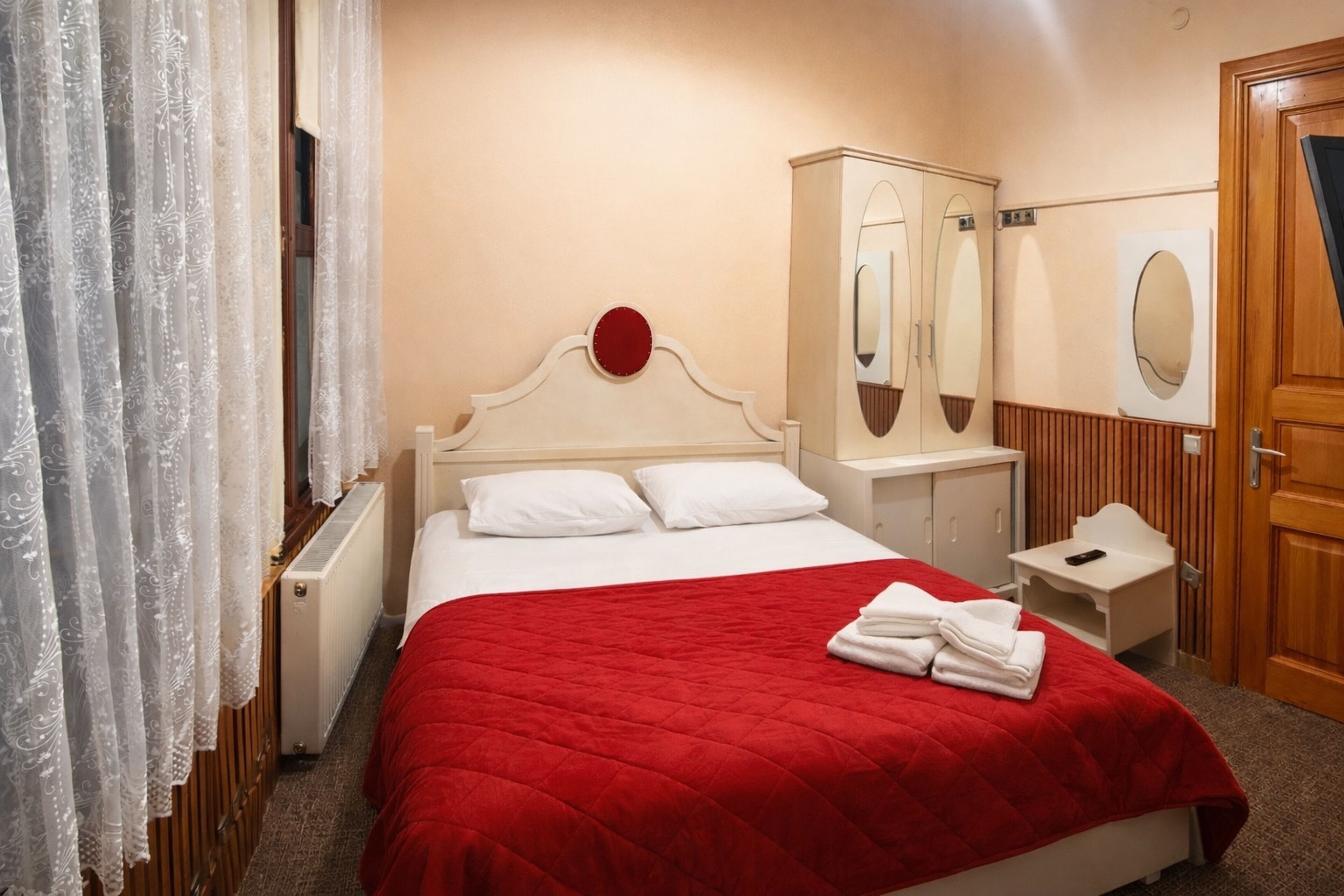 Una habitación de hotel con una cama, una mesita de noche, un espejo, un armario de madera y una puerta.