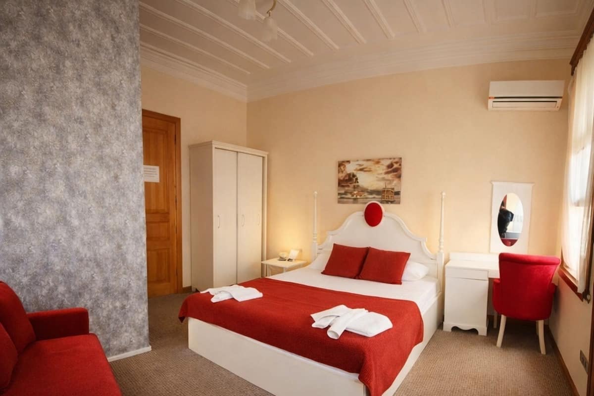 Une chambre d’hôtel avec un lit, une chaise rouge, un bureau et un appareil de climatisation.