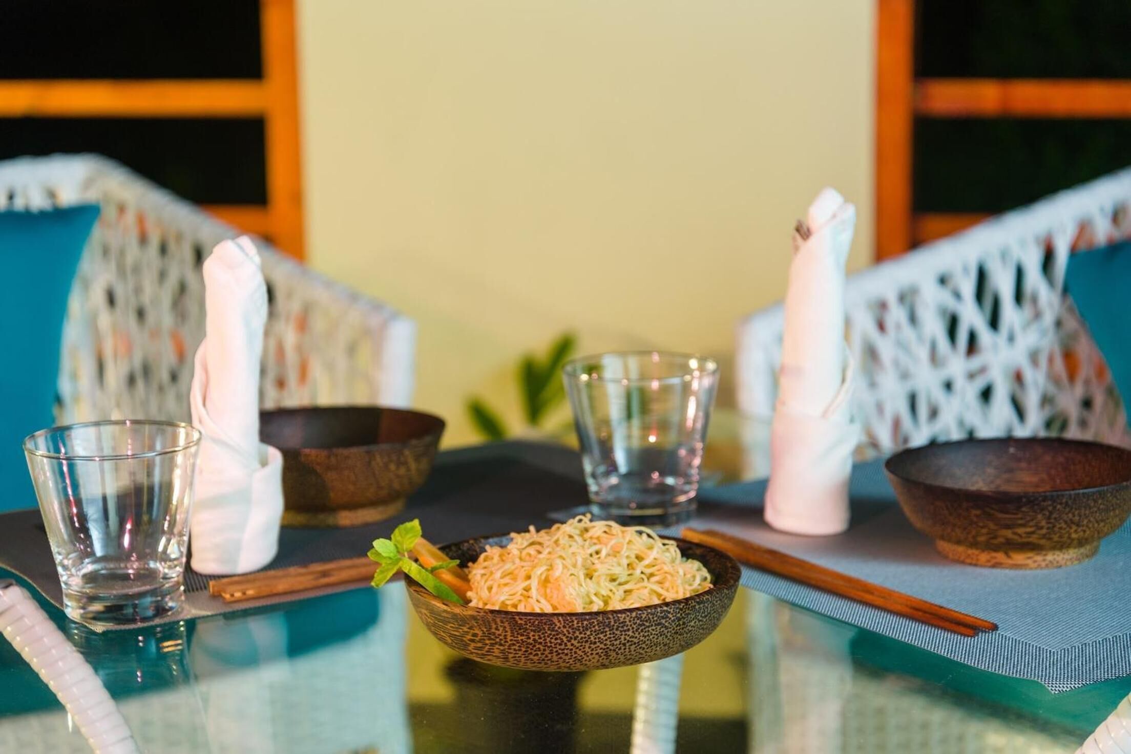 A dining table with a bowl of noodles, chopsticks, and two glasses.