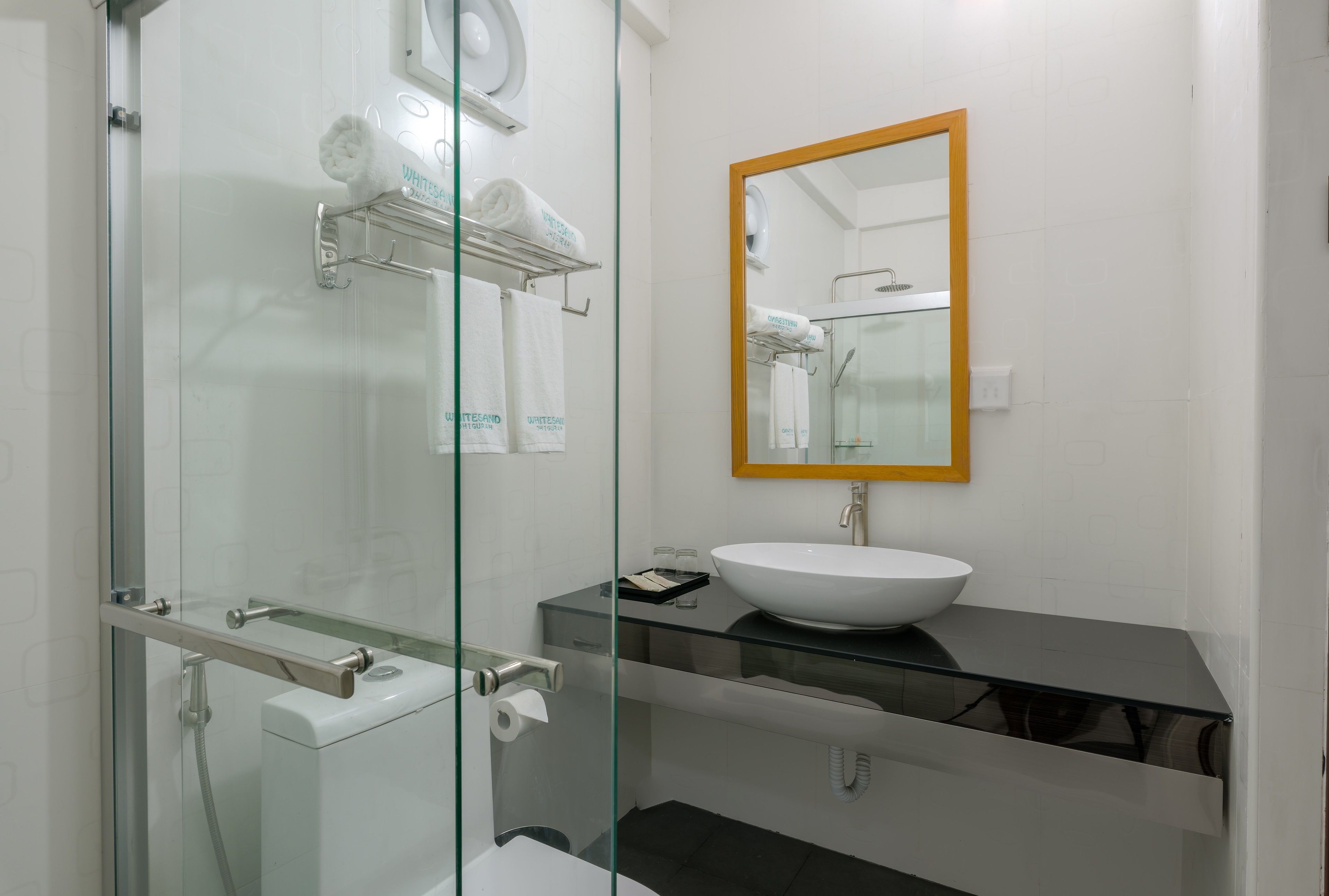 Un baño moderno con cabina de ducha de vidrio, un lavabo blanco y un espejo con marco de madera.