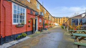 A narrow street with red brick buildings, outdoor seating, and a clear sky.