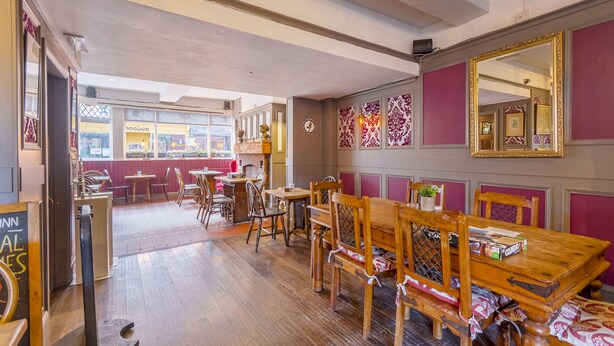 A restaurant interior with wooden tables and chairs, a large mirror, and decorative wall panels.