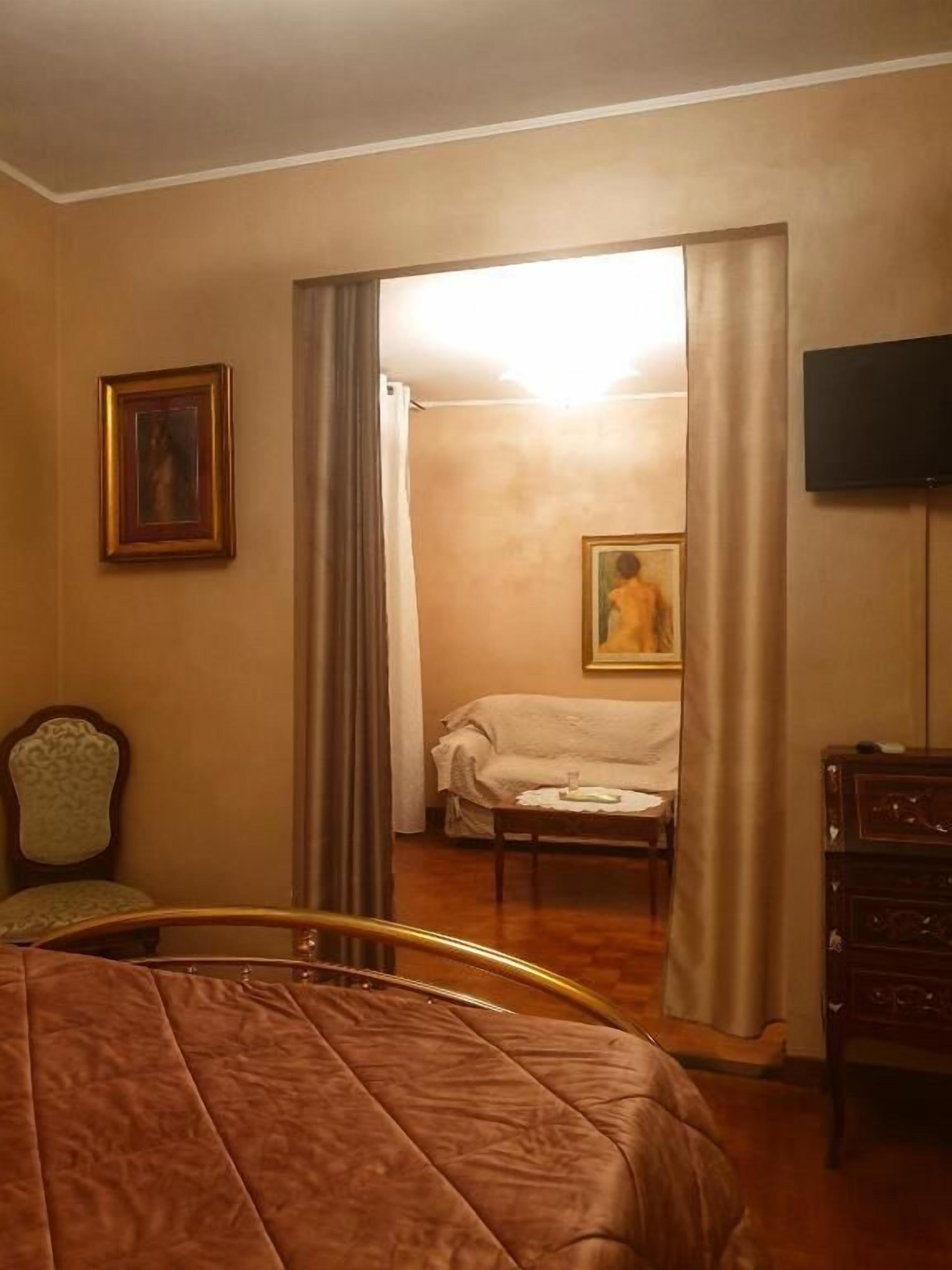 A hotel room with a bed, a chair, a desk, a television, and a painting on the wall.