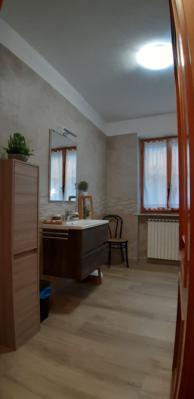 Een kleine kamer met een houten kast, een wastafel, een stoel en een raam met gordijnen.