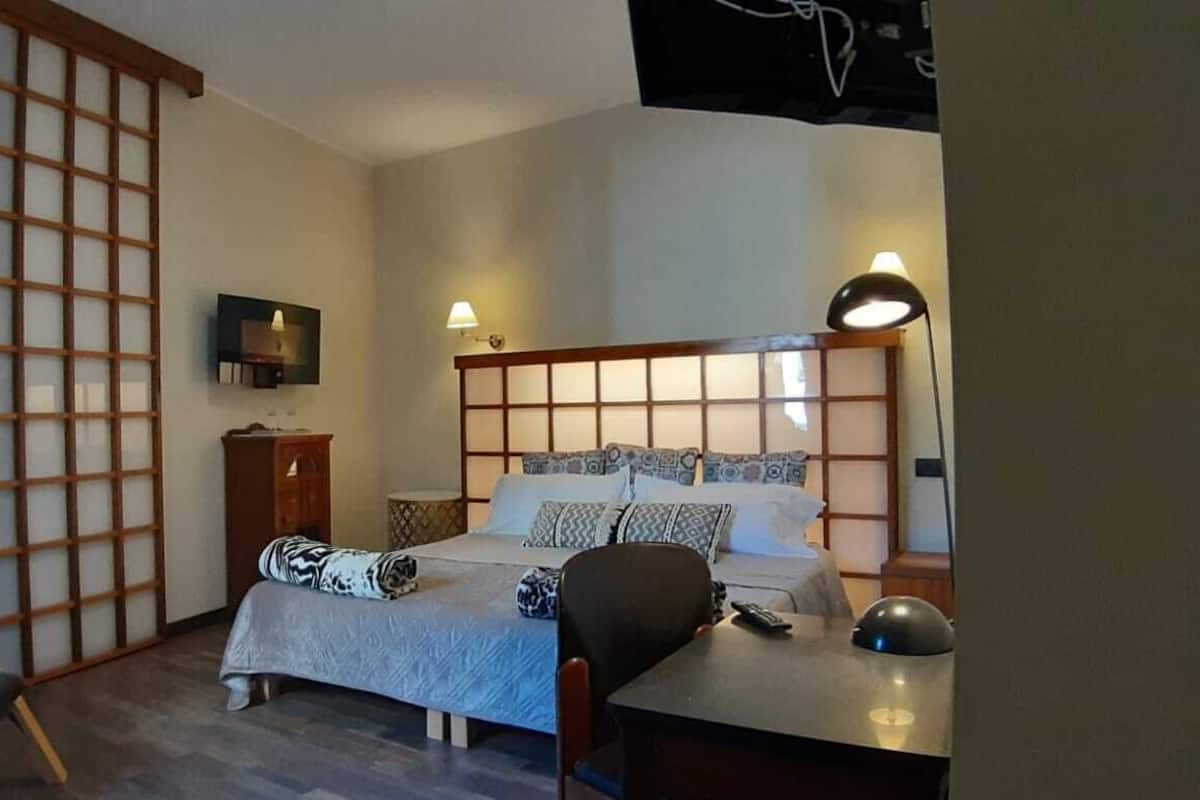 Habitación de hotel con cama, mesita de noche, silla y televisor en la pared.
