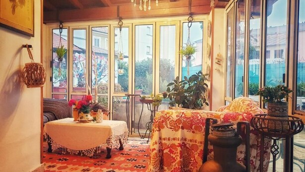 Um quarto aconchegante com teto de madeira, uma mesa com toalha de mesa florida e uma janela grande com plantas.