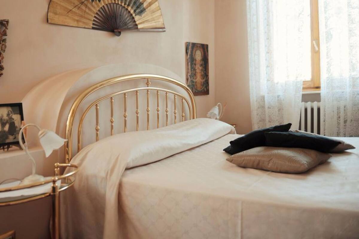 Un dormitorio con cama, mesita de noche, lámpara y un ventilador de pared.