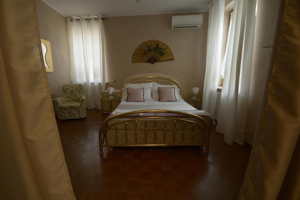 A bedroom with a bed, a chair, a bedside table, and a wall-mounted fan.