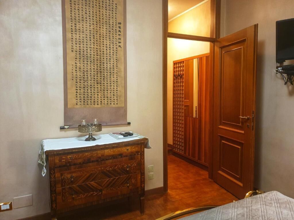 A room with a wooden cabinet, a wall-mounted decorative piece, a wooden door, and a television on the wall.
